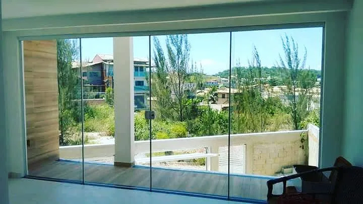 Sacada com fechamento de vidro frameless e vista para mata verde